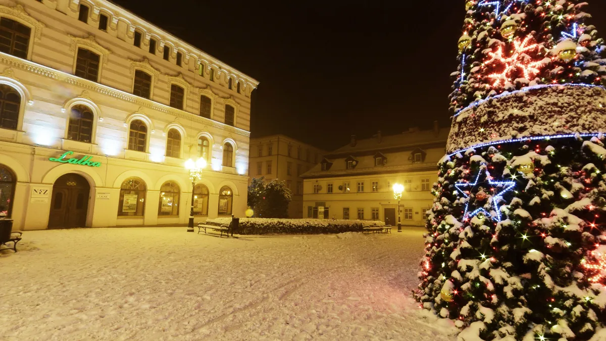 Zaśnieżony plac Piastowski w Cieplicach nocą, z oświetloną choinką