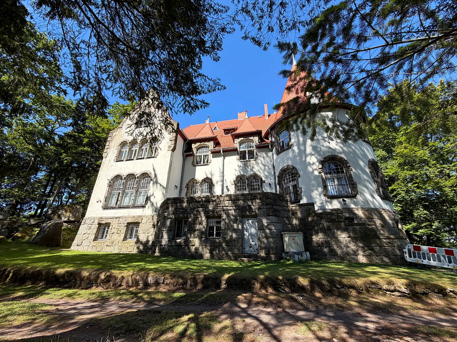 Willa Hauptmanna od strony ogrodu: wysoki kamienny cokół, rzędy okien w kamiennych obramieniach, wieżyczka z czerwonym dachem, wokół stare drzewa
